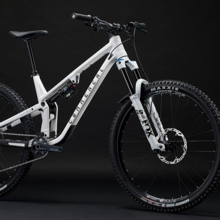 Vélo tout-terrain blanc sur fond noir, avec suspension avant et pneus crantés.